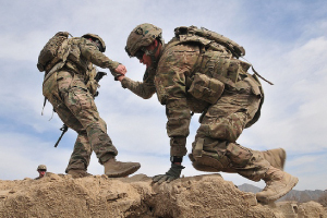 Service member helping another up a mountain