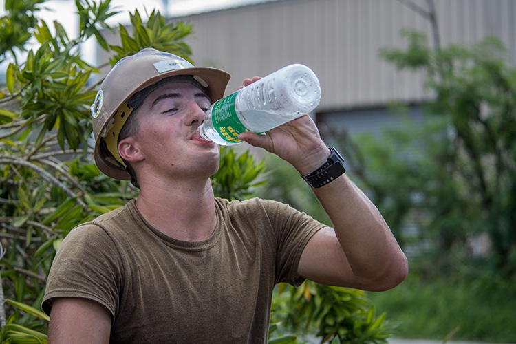 Image of Builder 3rd Class drinks water while reconstructing a roof for a home that was damaged during Typhoon Mangkhut.