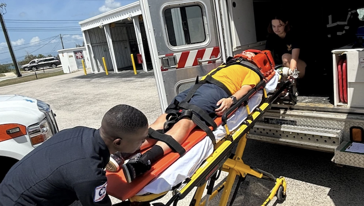 Military personnel practice loading a patient into an ambulance during training.