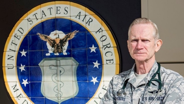 Image of Uniformed officer standing next to an Air Force seal, wearing a stethoscope around his shoulders.