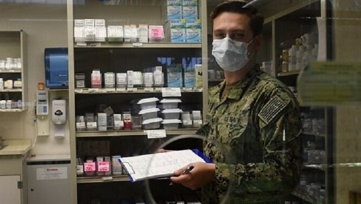 Image of Soldier wearing mask, marking items off in supply room.