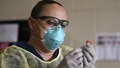 Medical personnel wearing a mask, looking at a vial