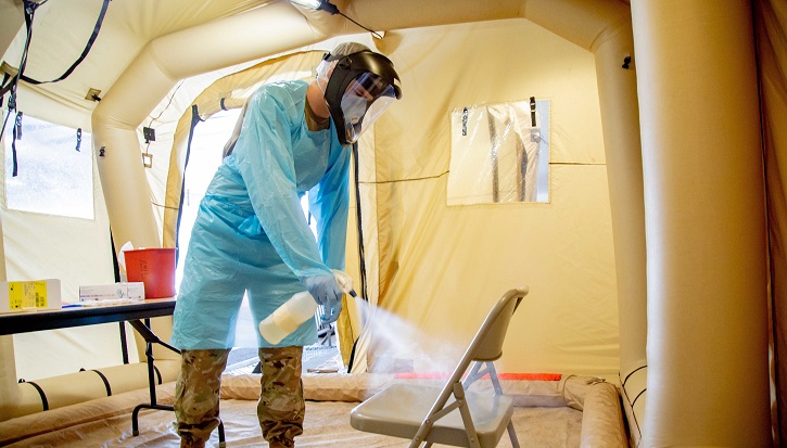 Man in full PPE spraying down a chair with sanitizer