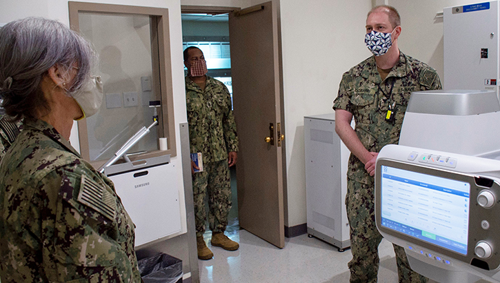 Image of Corpsman showing medical equipment to group of people in masks. Click to open a larger version of the image.
