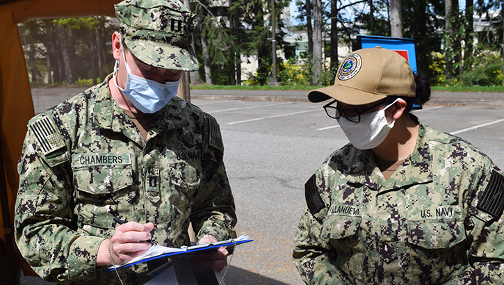 Masked Navy members consult clipboard.