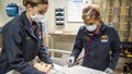 Two nurses, wearing masks, examining a mannequin