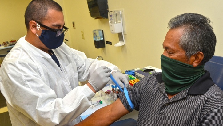 Image of Medical technician giving a man a vaccine shot; both wearing masks. Click to open a larger version of the image.