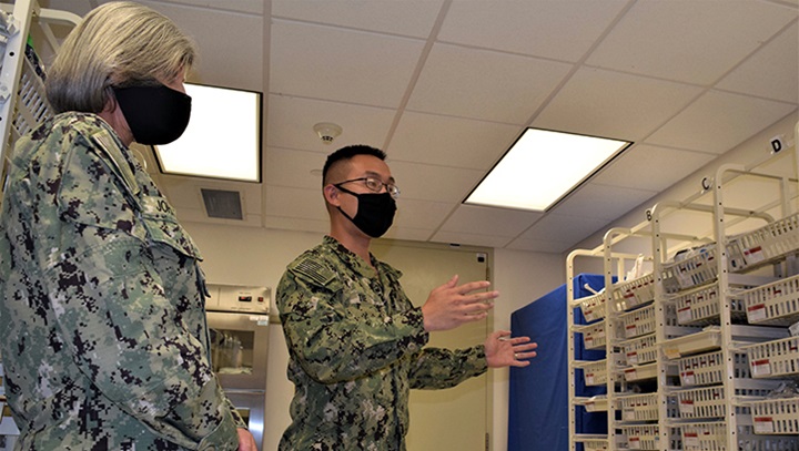 Image of Two military personnel, wearing masks, in a supply room looking at the shelves.