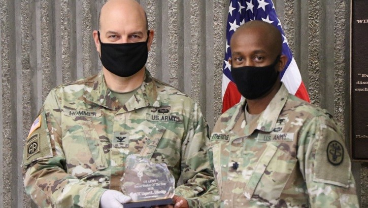 Two military personnel, wearing masks, holding a crystal award