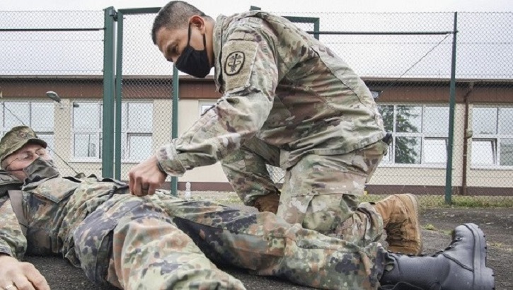 Image of Two soldiers, one laying on the ground and the other giving him medical attention. Click to open a larger version of the image.