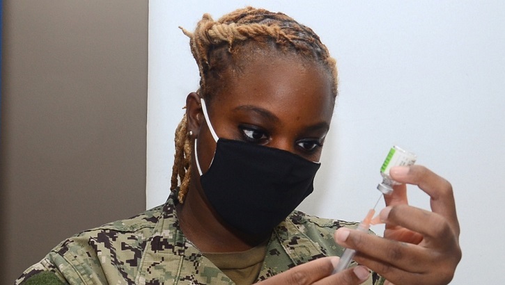 Image of Military personnel, wearing a mask, looking at a syringe and a vial. Click to open a larger version of the image.