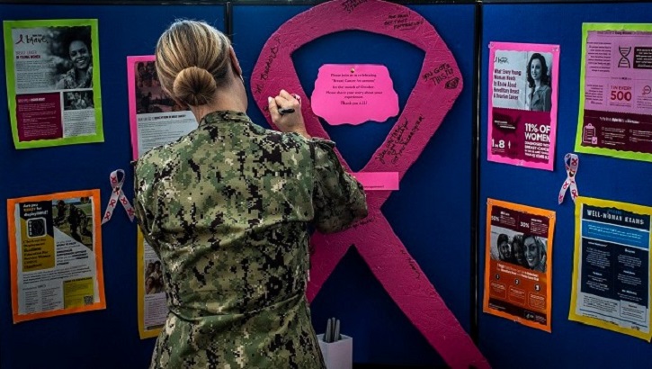 Image of Soldier standing in front of a colorful display with pink ribbon. Click to open a larger version of the image.