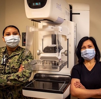 Two medical personnel wearing masks, standing next to a mammography machine