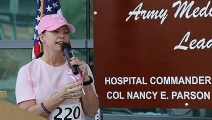 Woman in pink hat and shirt, wearing a racing number, speaking to an audience