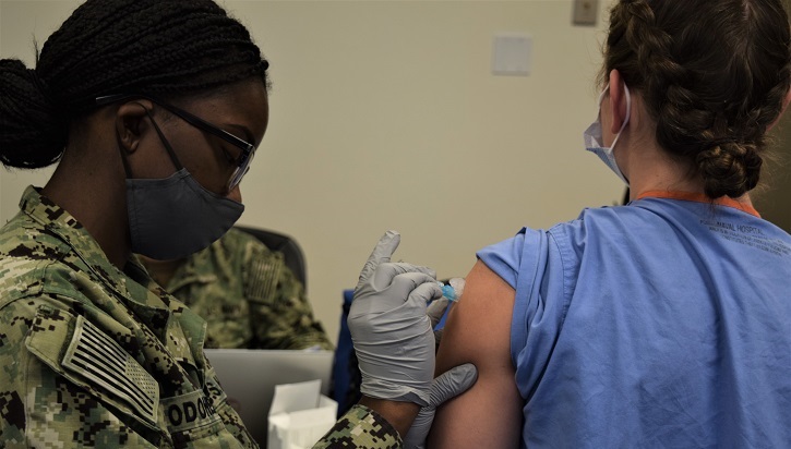 Military personnel giving patient a flu vaccine in her left arm