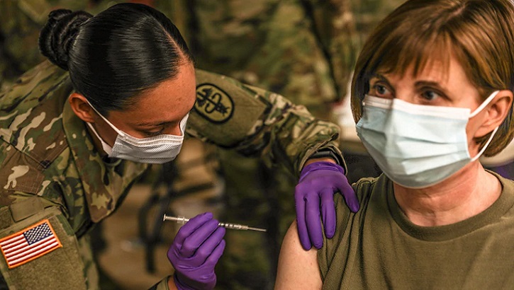 Military personnel giving a vaccine to a soldier in her right arm