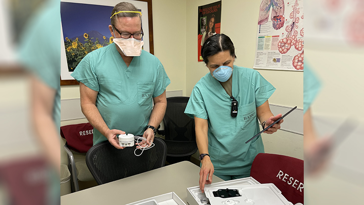 Image of Two medical personnel, wearing masks, looking at the contents of a home-based COVID treatment kit.
