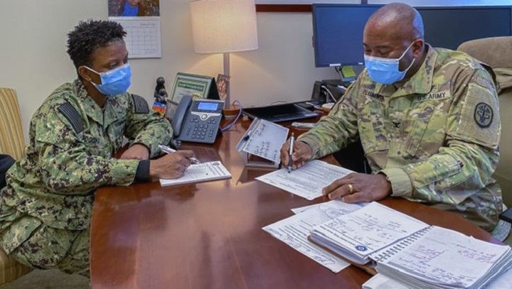 Image of Two military personnel, wearing masks, in a meeting.