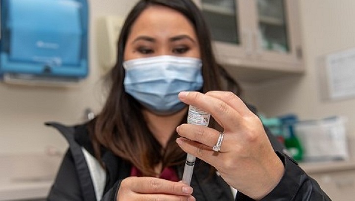 Image of a military healthcare worker holding a vaccine needle. Click to open a larger version of the image.