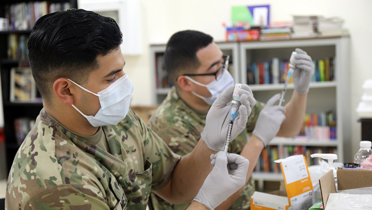 Image of Two healthcare workers, wearing masks, adding the COVID-19 vaccine to syringes. Click to open a larger version of the image.