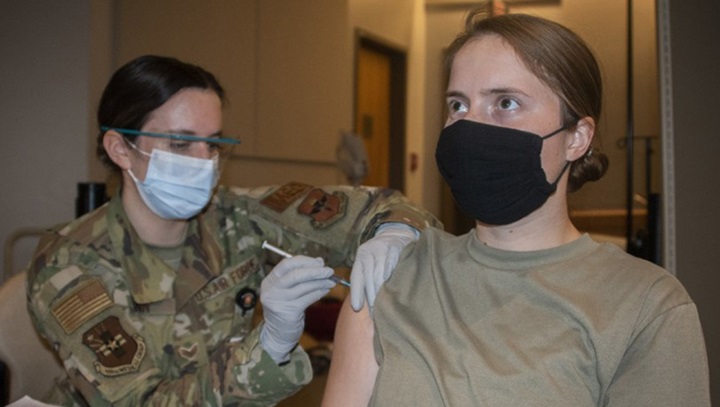 Image of Medical personnel giving a vaccine to a soldier in her right arm.