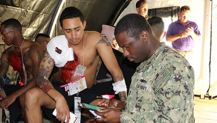 Image of An Army soldier and patient actor sports a mock impalement while providing simulated medical information to test out a new electronic medical record system designed to virtually document medical encounters in the field. The mock scenario was part of the U.S. Navy’s Rim of the Pacific exercise in 2018. (Photo: Ana Allen, U.S. Army).