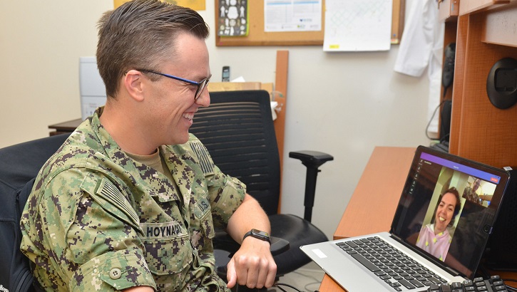 Military physician sitting at desk, talking to patient on his computer