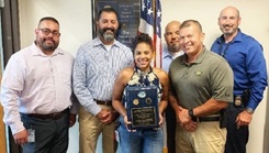 Woman holding award plaque, surrounded by colleagues