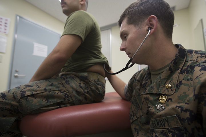 Image of A U.S. naval officer listens through his stethoscope to hear his patient’s lungs.