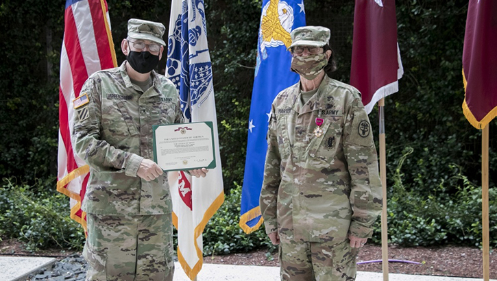 Two masked soldier display an award in front of flags.