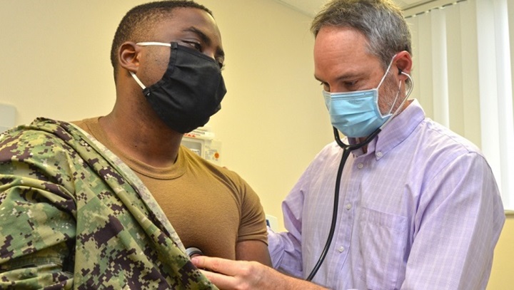 Image of Military personnel wearing a face mask, gets his heart checked out by military heath personnel.