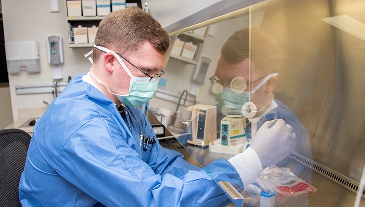 Image of Man in lab coat and mask prepares sample for COVID-19 testing.