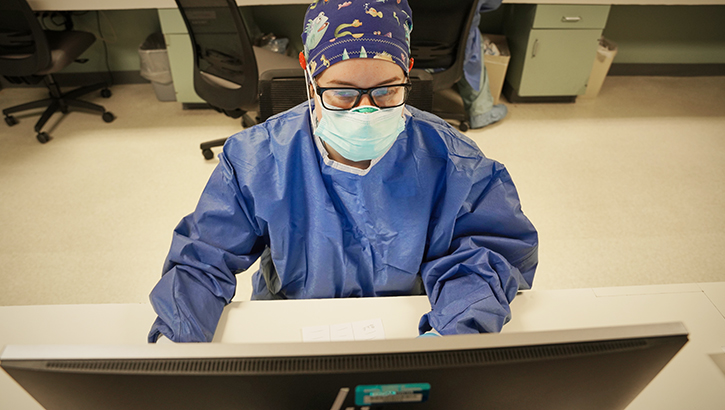 Clinician with mask looks at computer screen at a hospital.