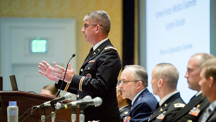 Military personnel speaking in front of an audience at the Military Health Systems Research Symposium