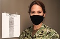 Image of Navy captain, wearing a mask, standing next to a piece of paper on the wall