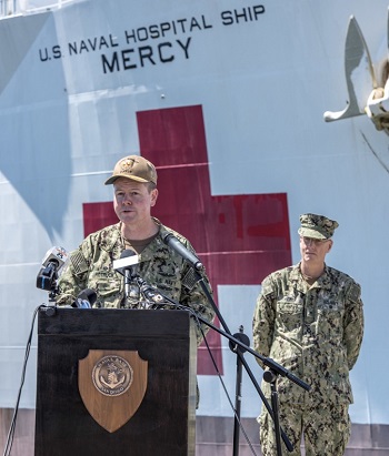 Captain Rotruck speaking at a podium in front of the USNS Mercy