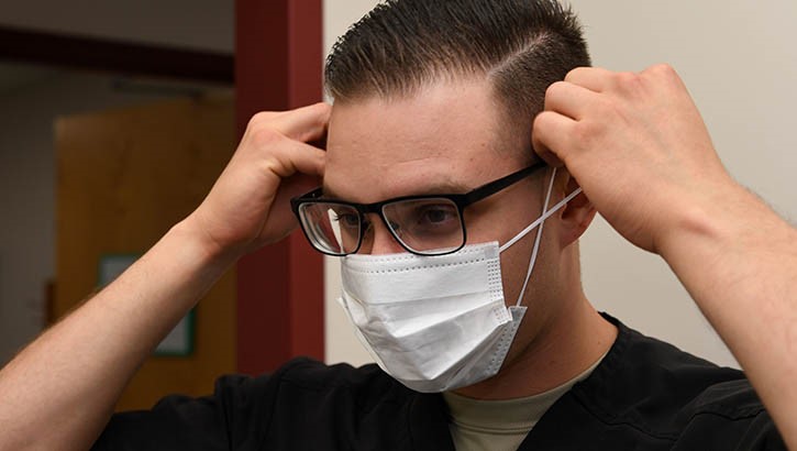 Um assistente dentário do 319º Grupo Médico, demonstra um procedimento sanitário adequado, colocando uma máscara facial nas instalações de tratamento médico da Base da Força Aérea de Grand Forks, ND