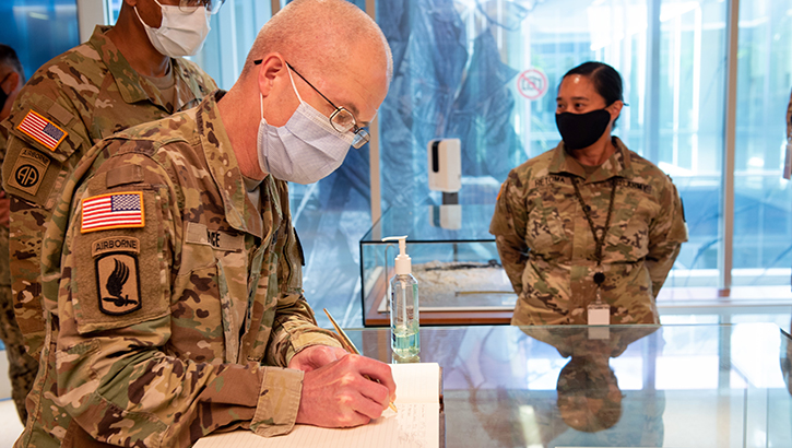 Image of Military Personnel wearing a face mask signing a book .