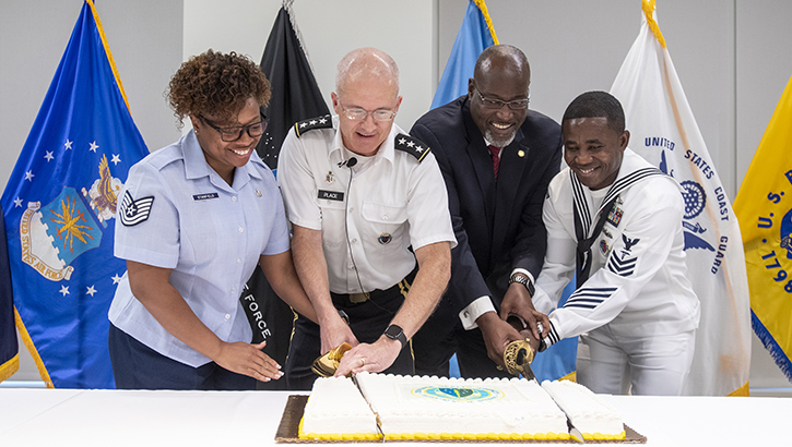 Four DHA personnel, including DHA Director Place, center, cut a birthday cake with a sword to celebrate DHA's ninth birthday. Oct. 1, 2022.