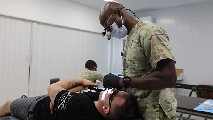 Image of Military health personnel wearing a face mask looking at someone's teeth.