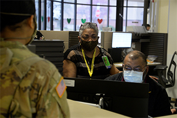 Military personnel wearing face mask looking at a computer