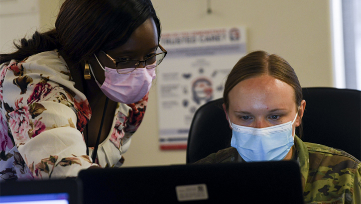 Image of Military health personnel wearing face mask looking at  a computer.