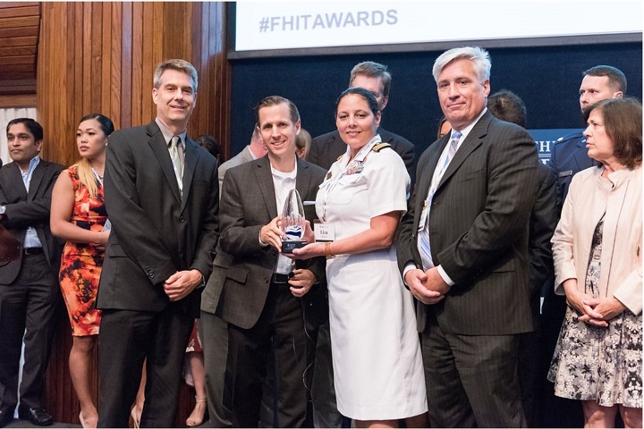 Defense Health Agency Tricare Online Patient Portal, Solution Delivery Division members Tim Larson (foreground, far left), Stan Adamus (foreground, second from right), and Navy Capt. Lisa Morris (foreground, center) receive the FedHealthIT Innovation Award from FedHealthIT  executive editor David Blackburn (foreground, second from left). (Courtesy photo by Chris Ferenzi)
