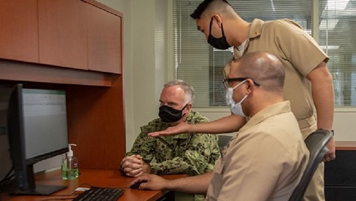 Three military personnel, wearing masks, in front of a computer screen