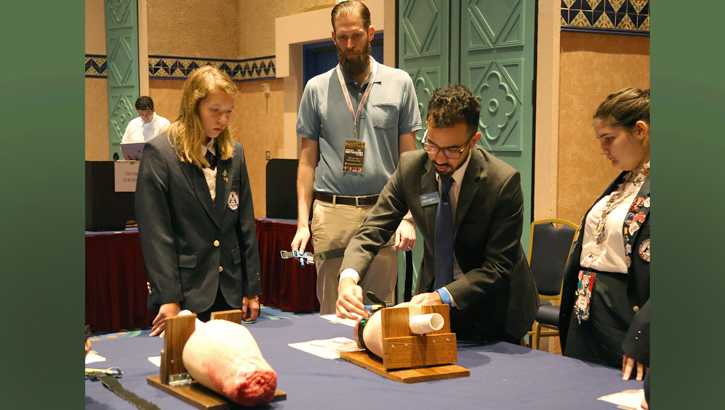 USU's Dr. Craig Goolsby (center) observes as high school students at a conference in Orlando, Florida, practice using a tourniquet after watching a web-based tutorial. Goolsby is researching effective teaching methods as part of a grant to develop a trauma first-aid course for students that incorporates elements of Stop the Bleed. (USU photo by Sarah Marshall)