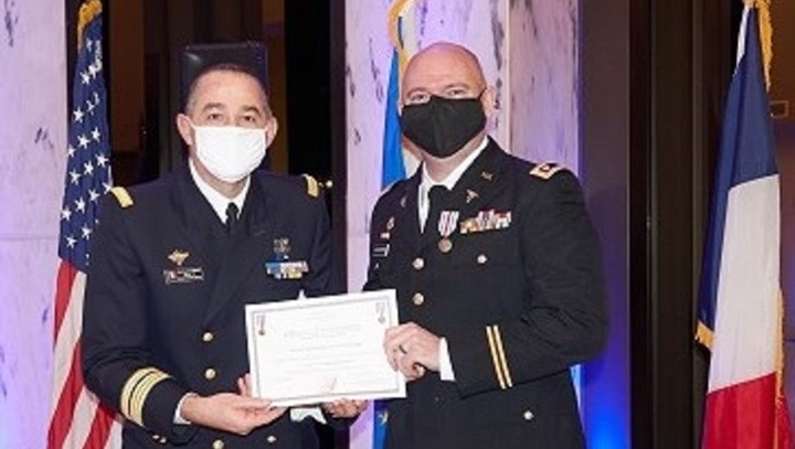 Image of Two military officers on stage; one handing the other a certificate.