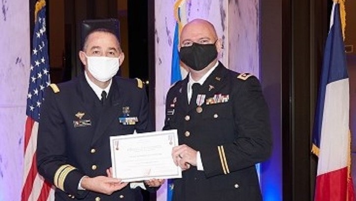 Two military officers on stage; one handing the other a certificate