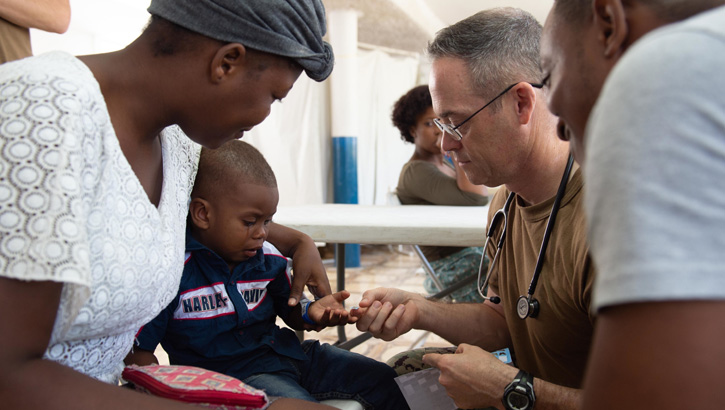 U.S. Navy Capt. Michael Sullivan, a pediatrician assigned to the hospital ship USNS Comfort, gives a sticker to a two-year-old boy after examining his skin infection at a temporary medical treatment site in Port-Au-Prince, Haiti. During Comfort’s deployment, the crew worked with health and government partners in Central America, South America, and the Caribbean to provide care on the ship and at a temporary medical treatment site, helping to relieve pressure on national medical systems, including those strained by an increase in cross-border migrants. (U.S. Navy Photo by Mass Communication Specialist 3rd Class Maria G. Llanos)