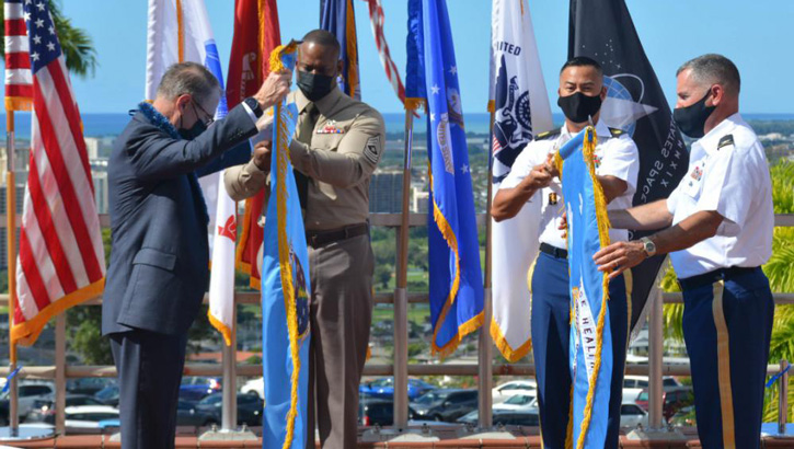 Image of DHA Assistant Director Dr. Brian Lein (left), and Hawaii Market Director Col. Martin Doperak (right) prepare to unfurl the flags during the formal Hawai'i Market Establishment Ceremony. Click to open a larger version of the image.