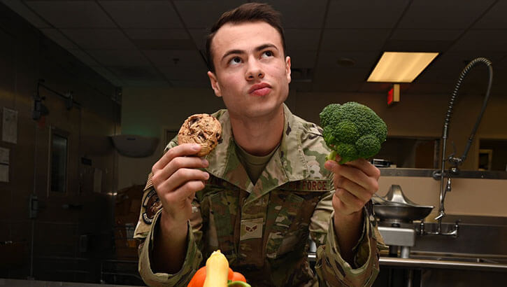 Image of Military personnel holding a cookie and broccoli.